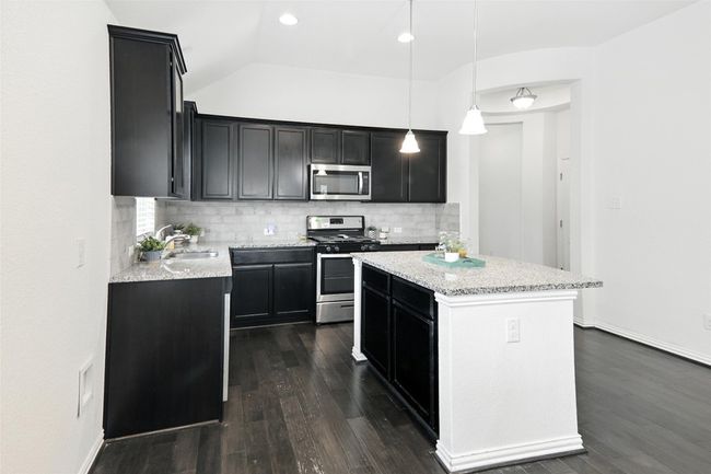 Kitchen featuring stainless steel appliances, dark cabinetry, dark wood-type flooring, tasteful backsplash, and a kitchen island | Image 12