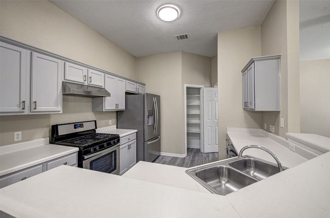 Kitchen with stainless steel appliances, under cabinet range hood, dark wood-type flooring, light countertops, and a textured ceiling | Image 8