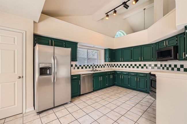 Kitchen featuring appliances with stainless steel finishes, a sink, vaulted ceiling, backsplash, and green cabinetry | Image 10