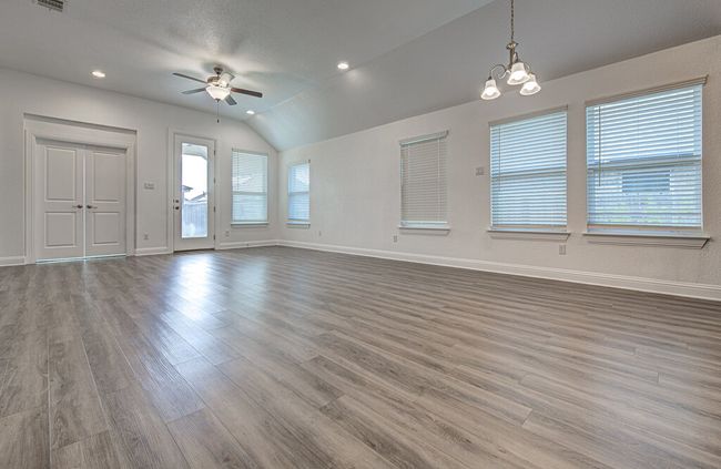Unfurnished living room featuring ceiling fan, vaulted ceiling, wood finished floors, baseboards, and a chandelier | Image 5