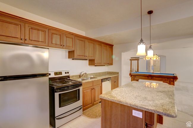 Kitchen with pendant lighting, light stone countertops, a kitchen island, appliances with stainless steel finishes, and a sink | Image 39