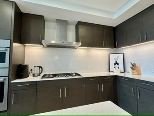 Kitchen featuring wall chimney exhaust hood, gas stovetop, light countertops, modern cabinets, and a tray ceiling | Image 18