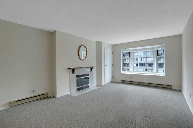 Unfurnished living room with baseboard heating, a baseboard heating unit, carpet floors, a tiled fireplace, and a textured ceiling | Image 4