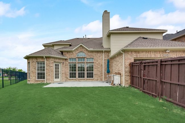 Rear view of property featuring brick siding, a chimney, a patio area, roof with shingles, and a garage | Image 23