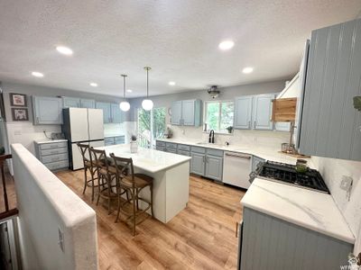 Kitchen with stainless steel dishwasher, white refrigerator, light LVP flooring, sink, and a center island | Image 2