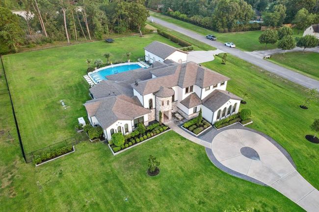 This photo shows a spacious, elegant home with a large swimming pool, set on a well-manicured lawn. The property features a circular driveway and is surrounded by greenery, offering privacy and a serene atmosphere. | Image 9