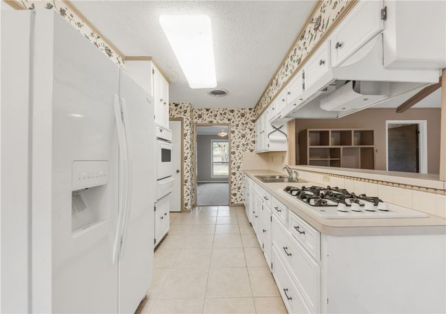 Kitchen featuring white appliances, wallpapered walls, a textured ceiling, light countertops, and white cabinets | Image 6