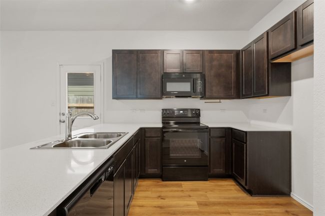 Kitchen featuring black appliances, light countertops, dark brown cabinetry, and light wood-type flooring | Image 19