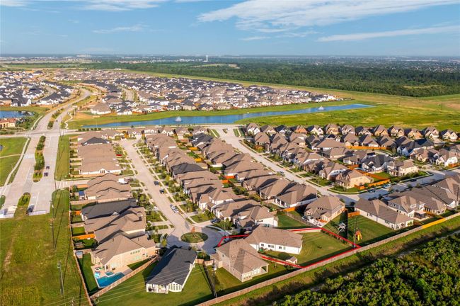 This aerial photo showcases a suburban neighborhood with neatly arranged houses, well-maintained lawns, and a network of roads. The area features a small body of water, offering a scenic touch. The community appears spacious and organized, with plenty of green space surrounding the homes. | Image 48