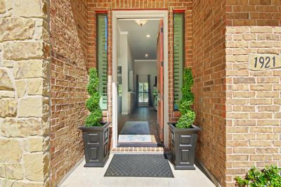 This photo shows a welcoming entrance with a natural wood door framed by brick walls, leading into a bright interior foyer. | Image 3