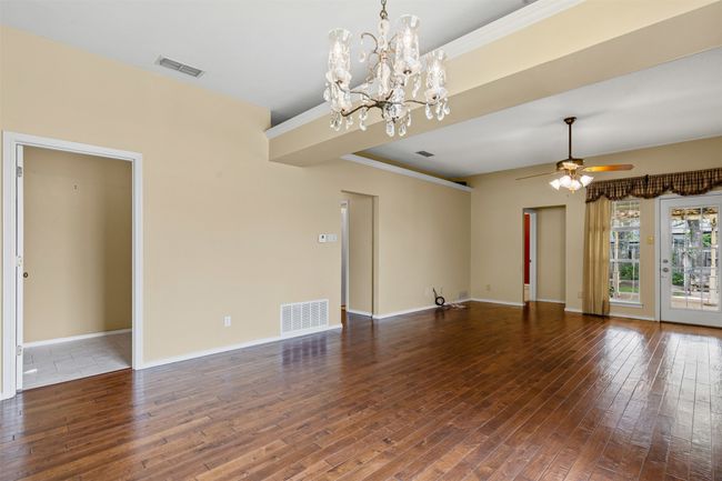 Open plan living room featuring plenty of natural light, wood-type flooring, a chandelier, ceiling fan, crown molding, and baseboards. | Image 11