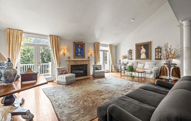Living area with wood finished floors, a fireplace with flush hearth, ornate columns, and high vaulted ceiling | Image 6