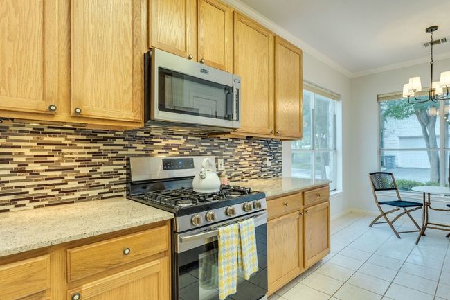Kitchen with appliances with stainless steel finishes, crown molding, light tile patterned floors, a chandelier, and tasteful backsplash | Image 15