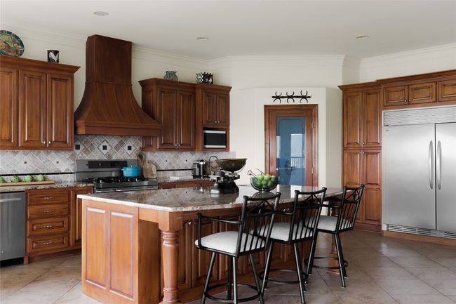 Kitchen featuring stainless steel appliances, premium range hood, stone counters, backsplash, and a kitchen breakfast bar | Image 21