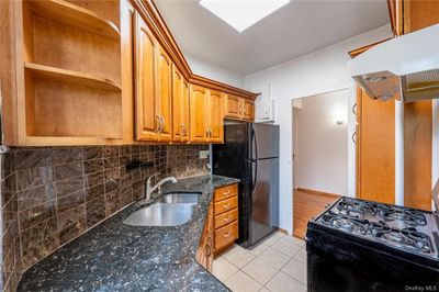 Kitchen with dark stone countertops, custom exhaust hood, light tile patterned floors, black appliances, and sink | Image 1