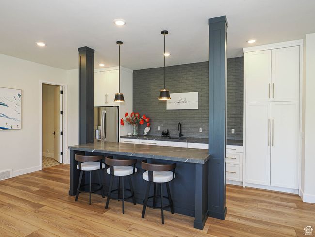 Kitchen featuring dark countertops, a breakfast bar, stainless steel refrigerator with ice dispenser, light wood-type flooring, and white cabinetry | Image 71