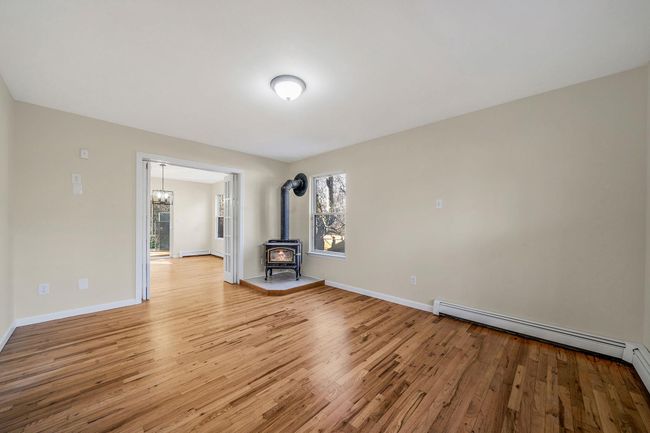 Unfurnished living room featuring a chandelier, a baseboard radiator, baseboards, light wood-style floors, and a wood stove | Image 6