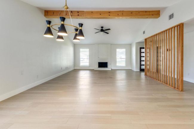 Unfurnished living room with visible vents, baseboards, light wood finished floors, a fireplace, and a notable chandelier | Image 10