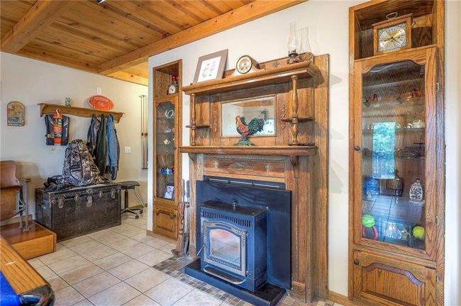 Living room with a wood stove, a wooden ceiling with exposed beams, and light tile patterned floors | Image 36