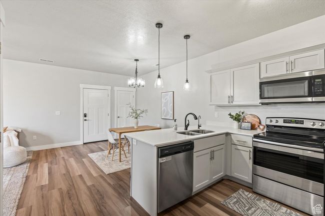 Kitchen featuring appliances with stainless steel finishes, hanging light fixtures, dark wood-style flooring, a peninsula, and a textured ceiling | Image 14