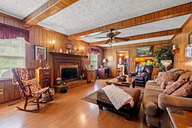 Living area featuring visible vents, wood finished floors, ceiling fan, wooden walls, and a fireplace | Image 6