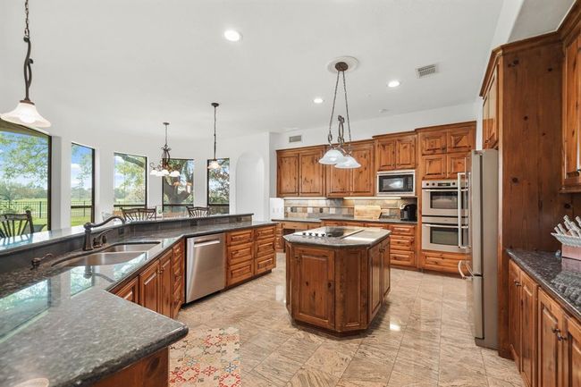 The centrally located island with lighting above serves home to a Bosch 5-burner glass cook top with downdraft ventilation. Additional appliances include double wall ovens, built-in microwave oven and a dishwasher. The dishwasher and both of the home's water heaters were replaced in 2024. | Image 14