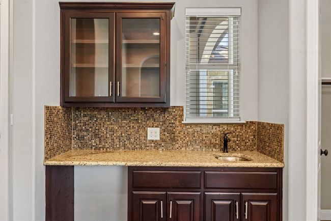 Bar featuring granite counters, decorative backsplash, glass insert cabinets, and dark brown cabinetry | Image 13