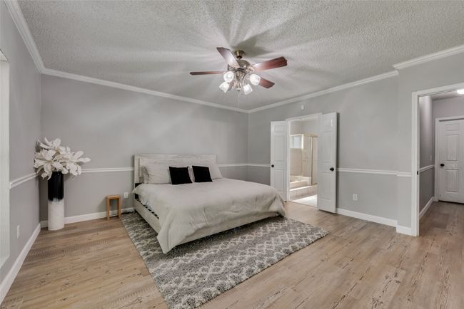 Bedroom with a textured ceiling, light wood-style flooring, ensuite bath, ornamental molding, and a ceiling fan | Image 15