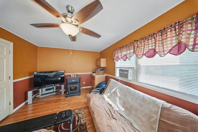Living area with a wood stove, wood finished floors, ceiling fan, baseboards, and cooling unit | Image 7