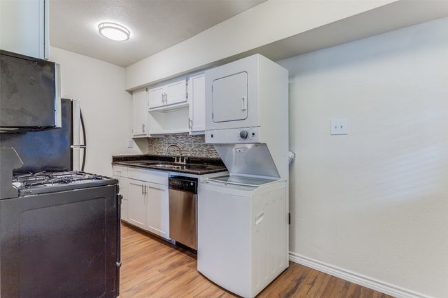 Kitchen featuring appliances with stainless steel finishes, stacked washer / drying machine, baseboards, decorative backsplash, and light wood-style floors | Image 5