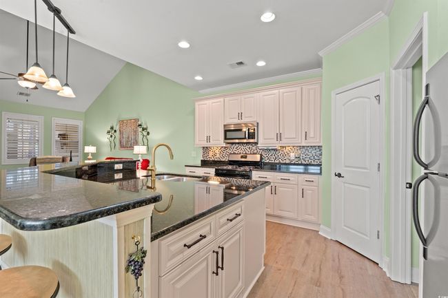 Kitchen with a kitchen bar, a sink, light wood finished floors, visible vents, and appliances with stainless steel finishes | Image 9