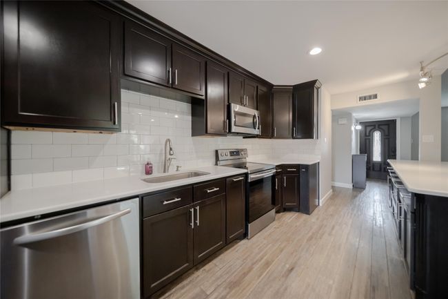 Kitchen featuring stainless steel appliances, light countertops, light wood-style floors, backsplash, and dark brown cabinetry | Image 11