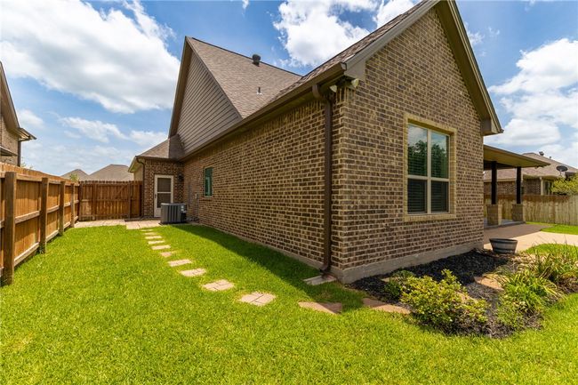 Follow the stepping stones to the side of the home, where you'll find access to the AC unit, a convenient door to the garage, and additional decking—perfect for storing garbage bins or other outdoor essentials. | Image 32