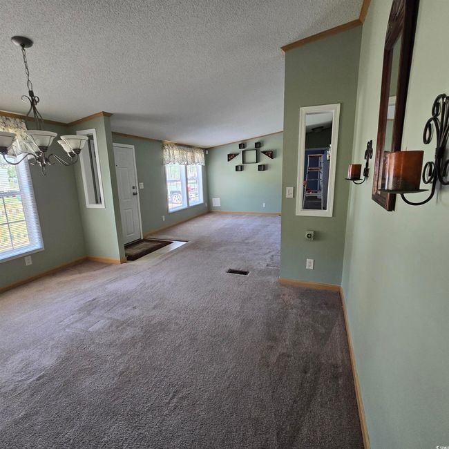 Unfurnished living room with a chandelier, crown molding, carpet, and a textured ceiling | Image 11