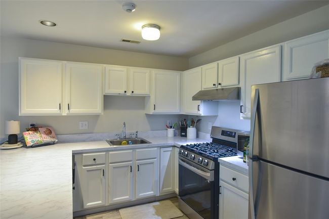 Kitchen featuring stainless steel appliances, a sink, under cabinet range hood, light countertops, and white cabinets | Image 8