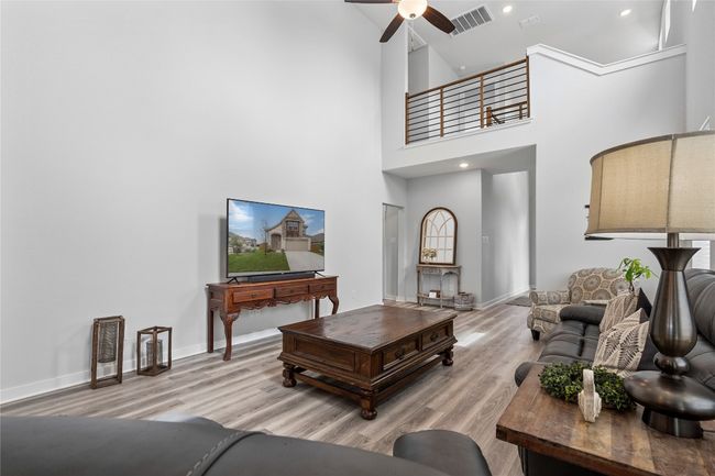 Living room featuring wood finished floors, a ceiling fan, a high ceiling, baseboards, and recessed lighting | Image 10