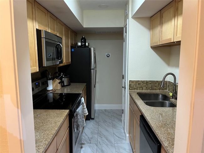 Kitchen with black electric range oven, stainless steel microwave, dishwasher, light marble finish floors, and decorative backsplash | Image 15
