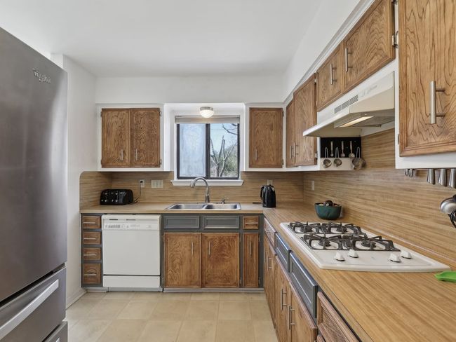 Kitchen with white appliances, under cabinet range hood, light countertops, a sink, and backsplash | Image 9