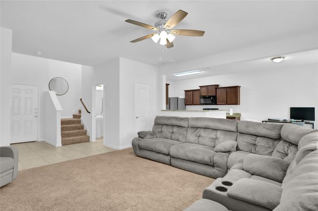 Living room featuring ceiling fan, stairway, light carpet, light tile patterned flooring, and baseboards | Image 8