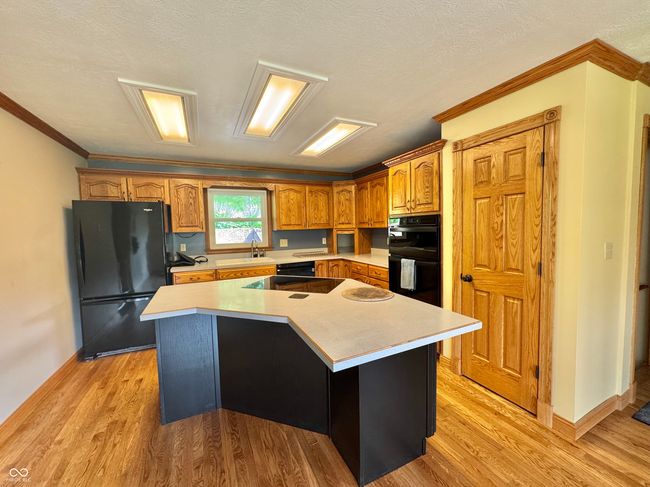 kitchen featuring black appliances, a sink, light countertops, light wood finished floors, and ornamental molding | Image 43
