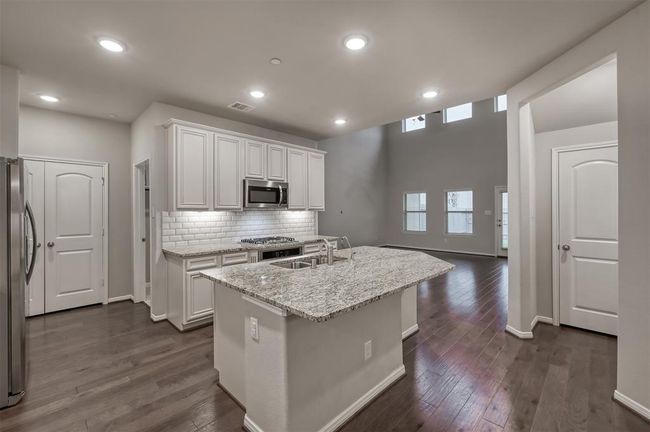 Modern kitchen with white cabinets, stainless steel appliances, granite countertops, subway tile backsplash, and hardwood floors with an open floor plan... | Image 5