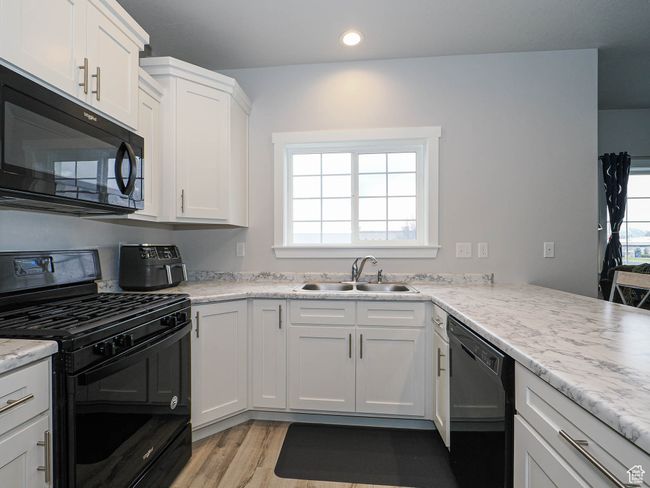 Kitchen with recessed lighting, a sink, light wood finished floors, white cabinets, and black appliances | Image 14