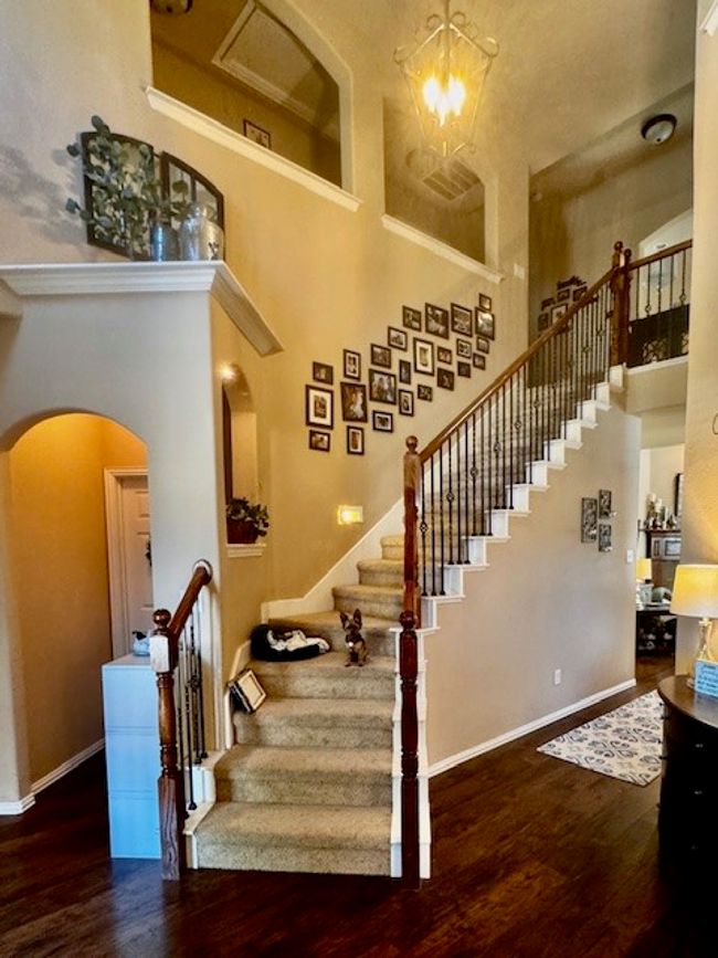Stairs featuring baseboards, arched walkways, a chandelier, wood finished floors, and a towering ceiling | Image 13