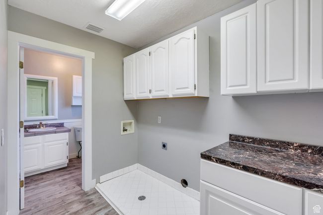 Laundry area featuring light wood finished floors, a sink, electric dryer hookup, cabinet space, and washer hookup | Image 18