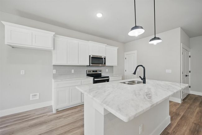 Kitchen with a sink, white cabinetry, light wood-type flooring, stainless steel appliances, and decorative backsplash | Image 4
