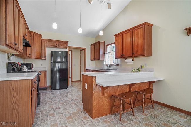 Kitchen featuring brown cabinets, under cabinet range hood, light countertops, black appliances, and a peninsula | Image 19