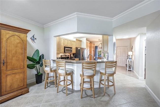 Kitchen with appliances with stainless steel finishes, a kitchen breakfast bar, crown molding, a peninsula, and light tile patterned floors | Image 8