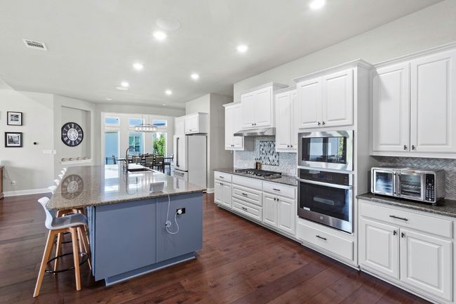 Kitchen with appliances with stainless steel finishes, tasteful backsplash, dark wood finished floors, an island with sink, and white cabinetry | Image 8
