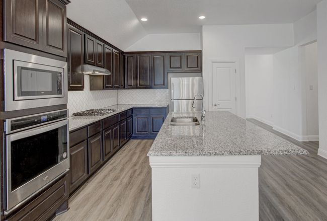 Kitchen with stainless steel appliances, a sink, light wood finished floors, a center island with sink, and dark brown cabinetry | Image 10