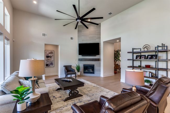 Living area with a high ceiling, a ceiling fan, a tile fireplace, wood finished floors, and recessed lighting | Image 11